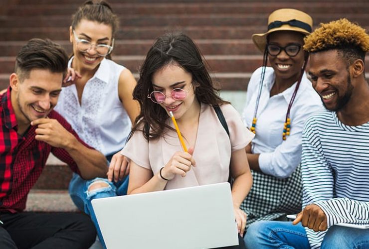 A group of people sitting on steps looking at a laptop.