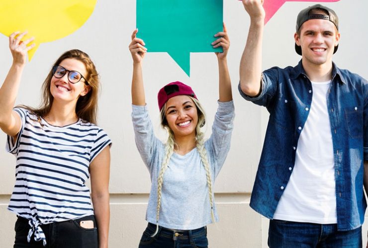 Three people holding up a green sign in front of them.