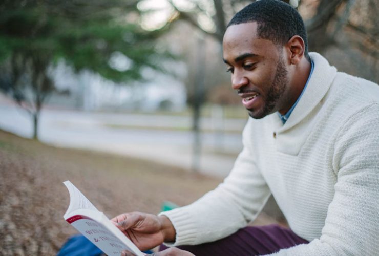 A man sitting on the ground reading a book.
