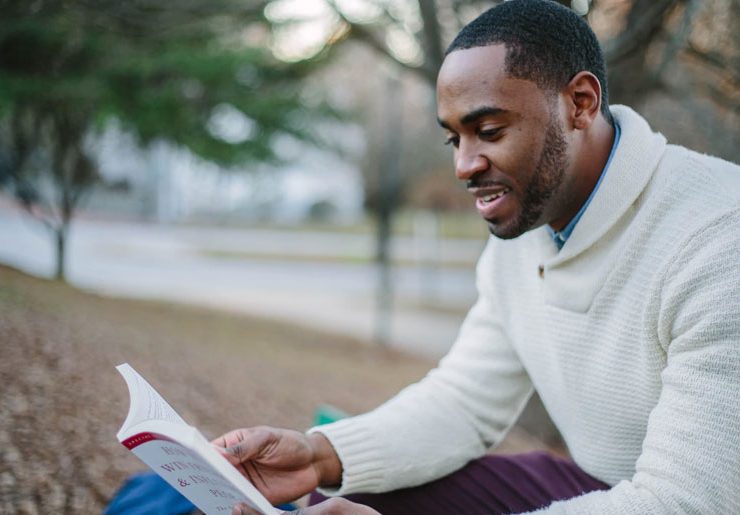 A man sitting on the ground reading a book.