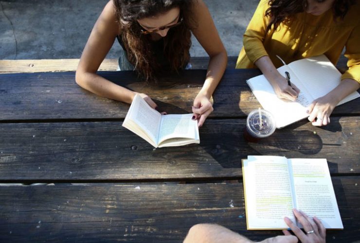 A group of people sitting at a table reading books.