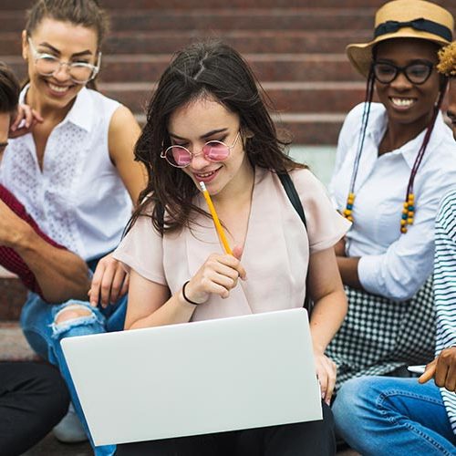 A group of people sitting on steps looking at a laptop.