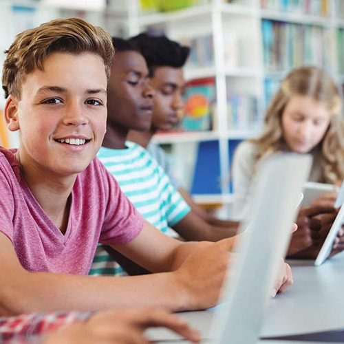 A group of kids sitting at a table with laptops.