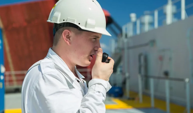 A man in white shirt and hard hat talking on a walkie talkie.