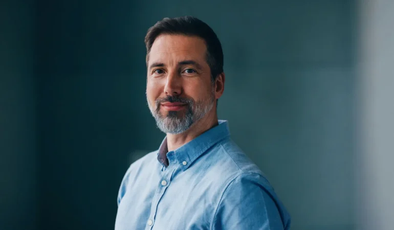 Middle-aged man with beard wearing a light blue shirt, smiling.
