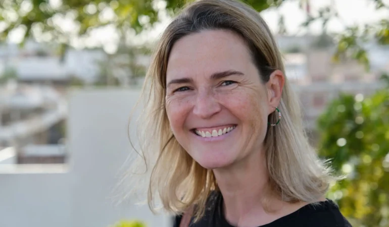 A woman smiling outdoors with a blurred background.
